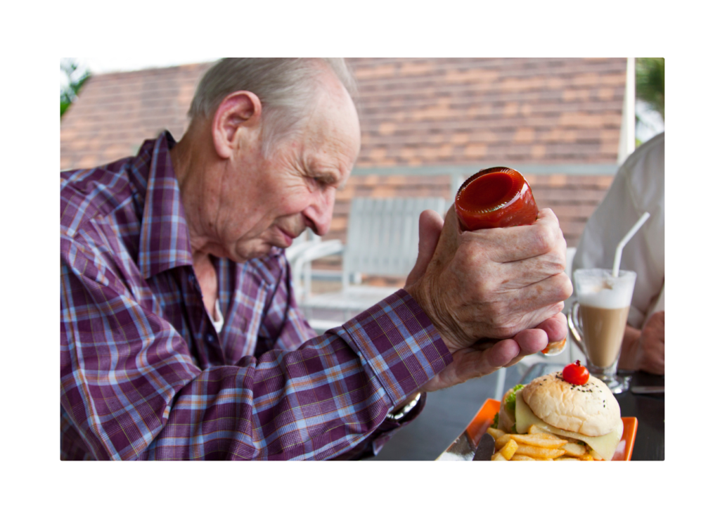 An elderly man applying force to a ketchup bottle, demonstrating Newton's First Law where an object at rest (the ketchup) stays at rest until acted upon by an external force.