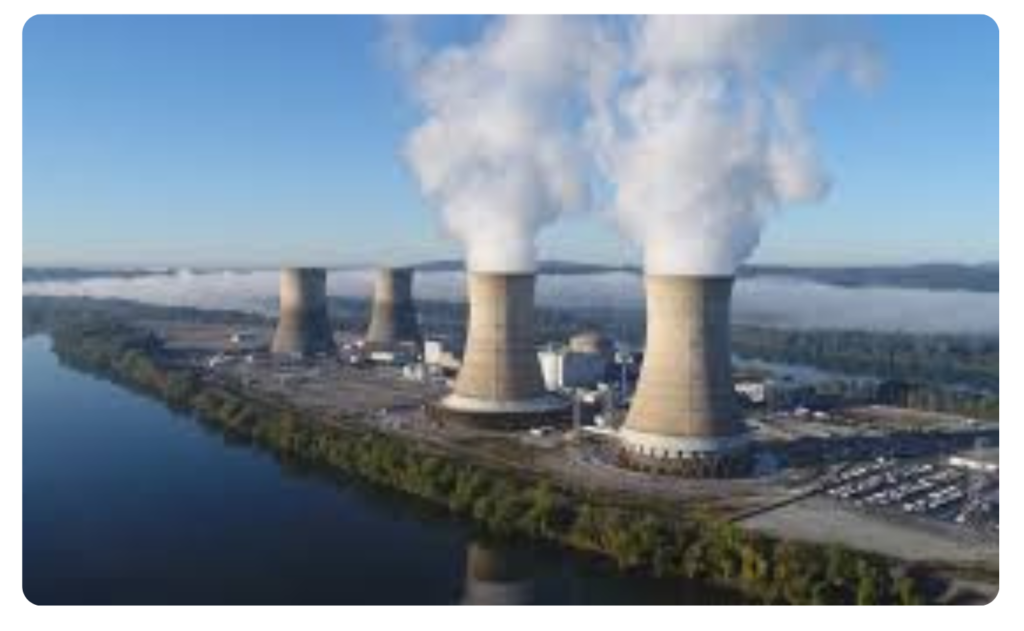 Aerial view of a nuclear power plant with large cooling towers emitting steam near a river